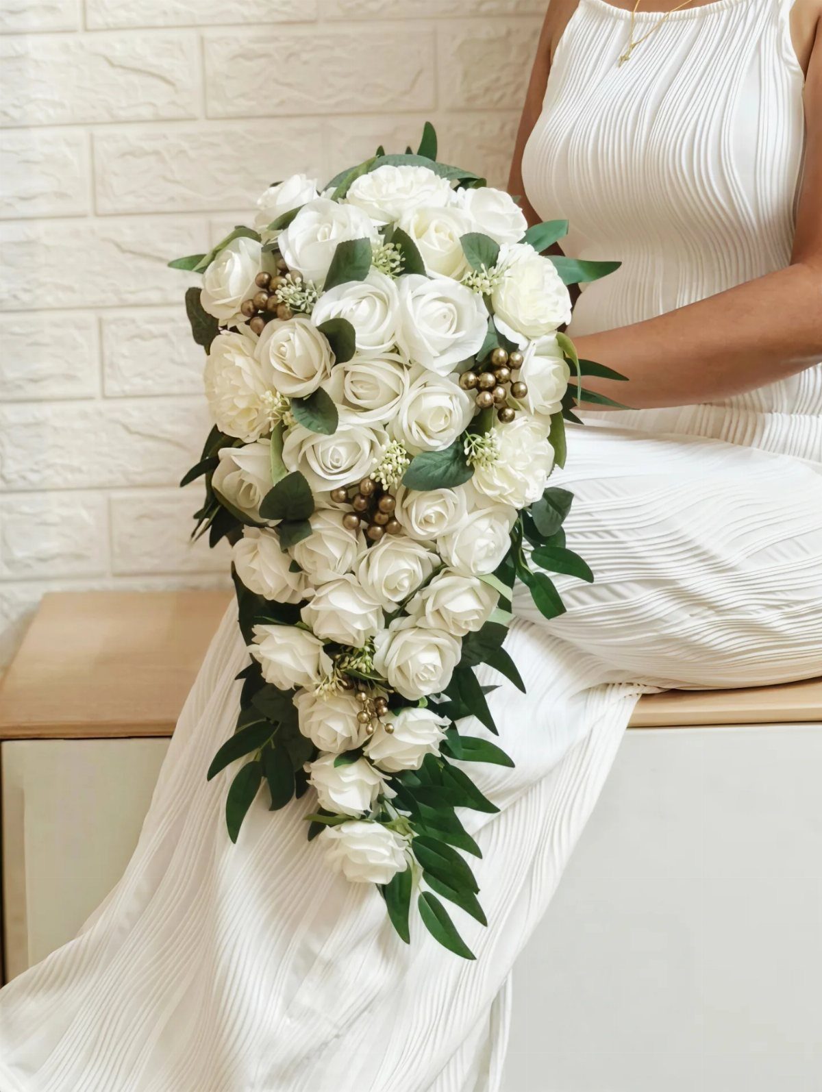 Cascading bridal bouquet of white roses and greenery held by a bride