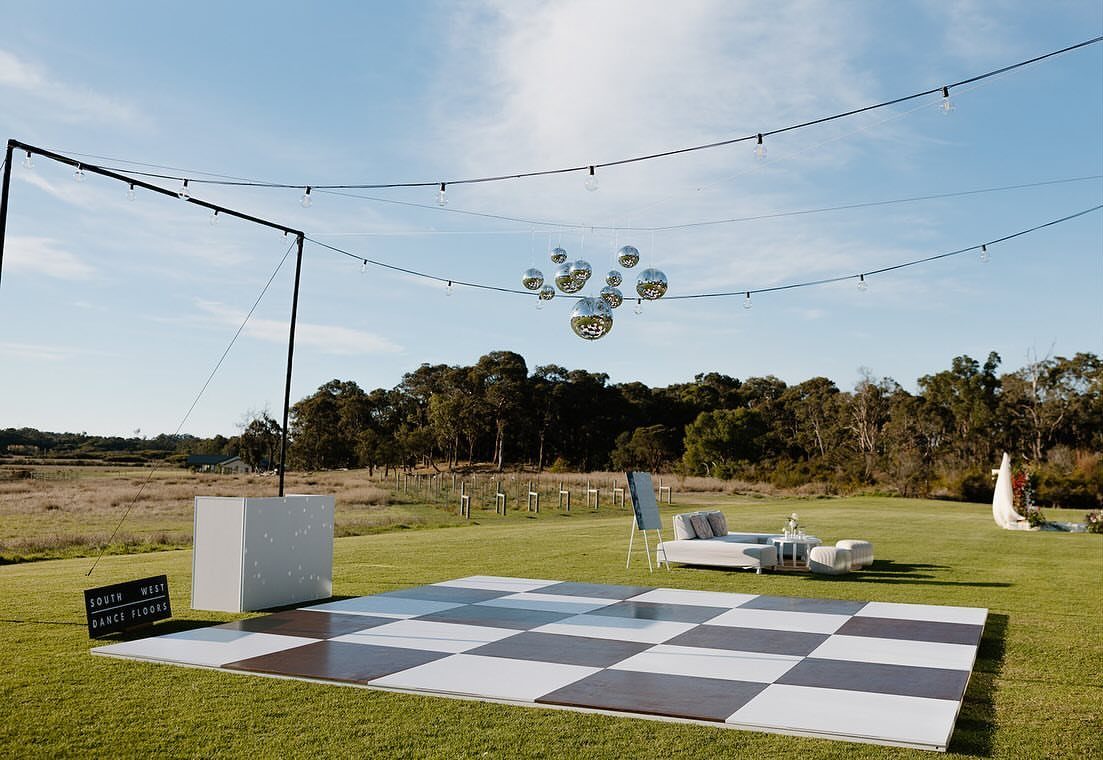 Black and white checkered dance floor on a grassy field with overhead disco balls.