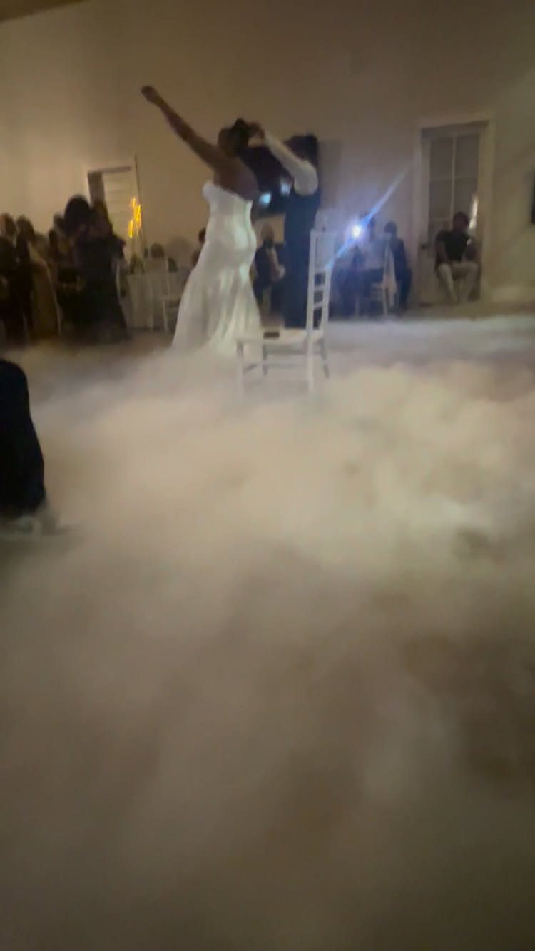 Bride and groom dancing in a room filled with low-lying white fog.