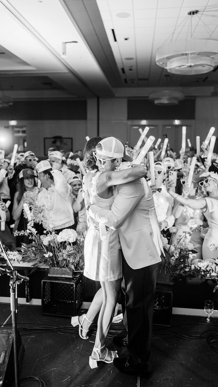 Couple embracing on a stage while guests hold white glow sticks in background
