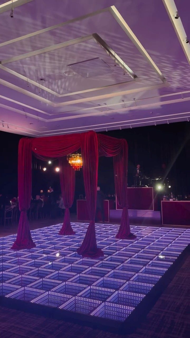 LED dance floor with white grid lighting under a red fabric canopy and chandelier.