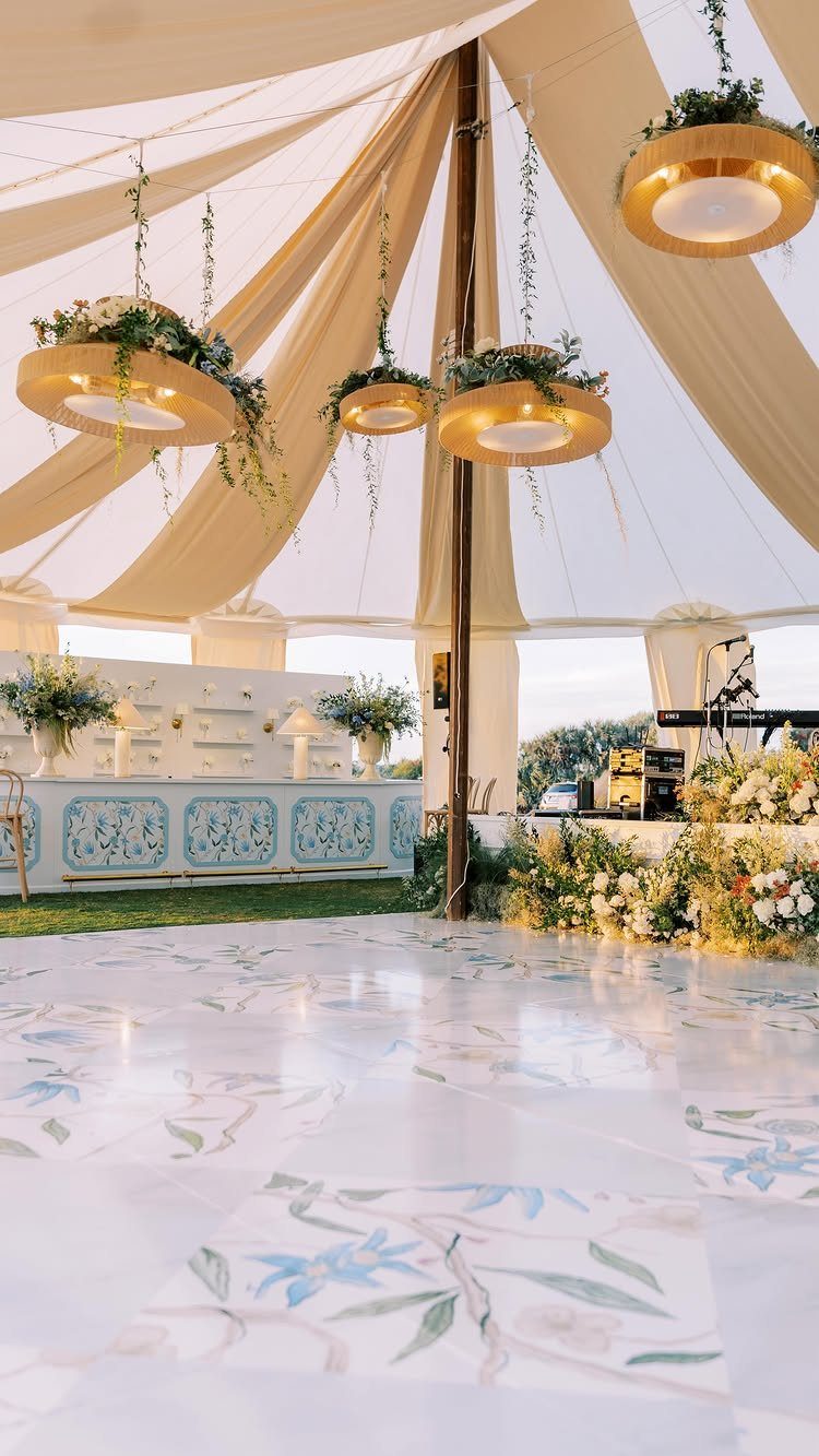 White floral patterned dance floor under a beige tent with gold chandeliers