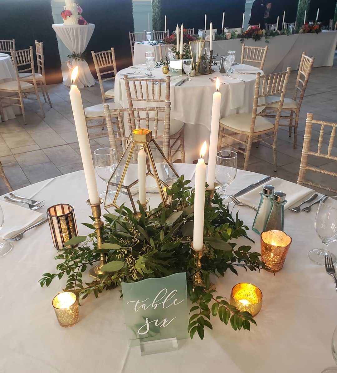 Wedding table centerpiece with deep green Italian Ruscus foliage and white taper candles.