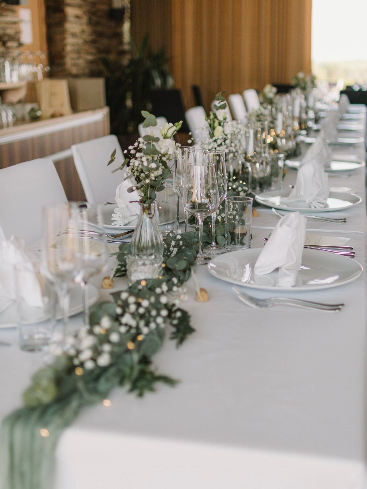 Seeded eucalyptus greenery runner with white flowers on a white wedding table.