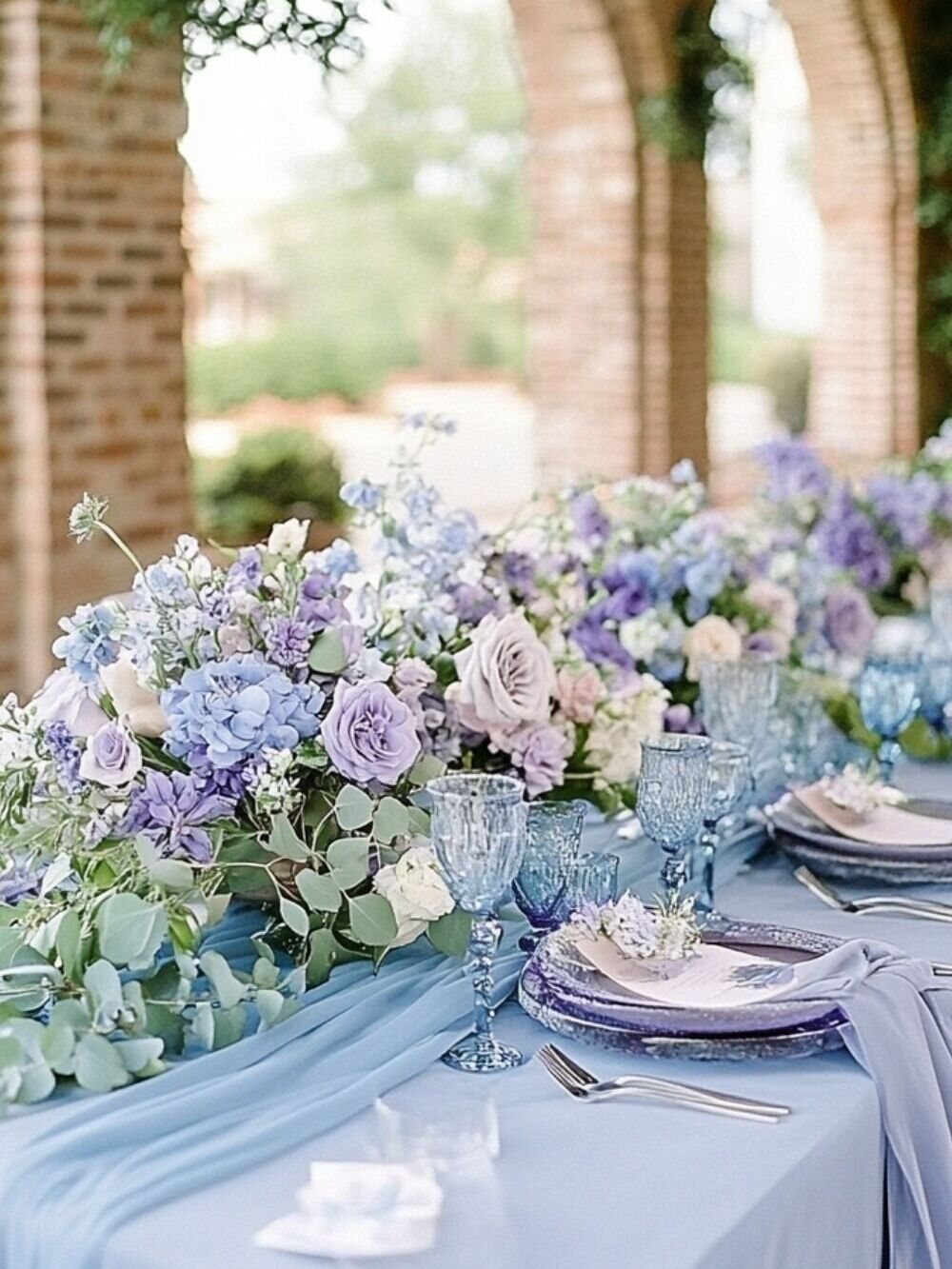 Dusty blue floral centerpieces and table settings on a light blue wedding table.