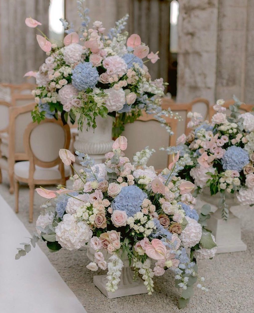 Floral arrangements with dusty blue hydrangeas and dusty rose roses in white urns.