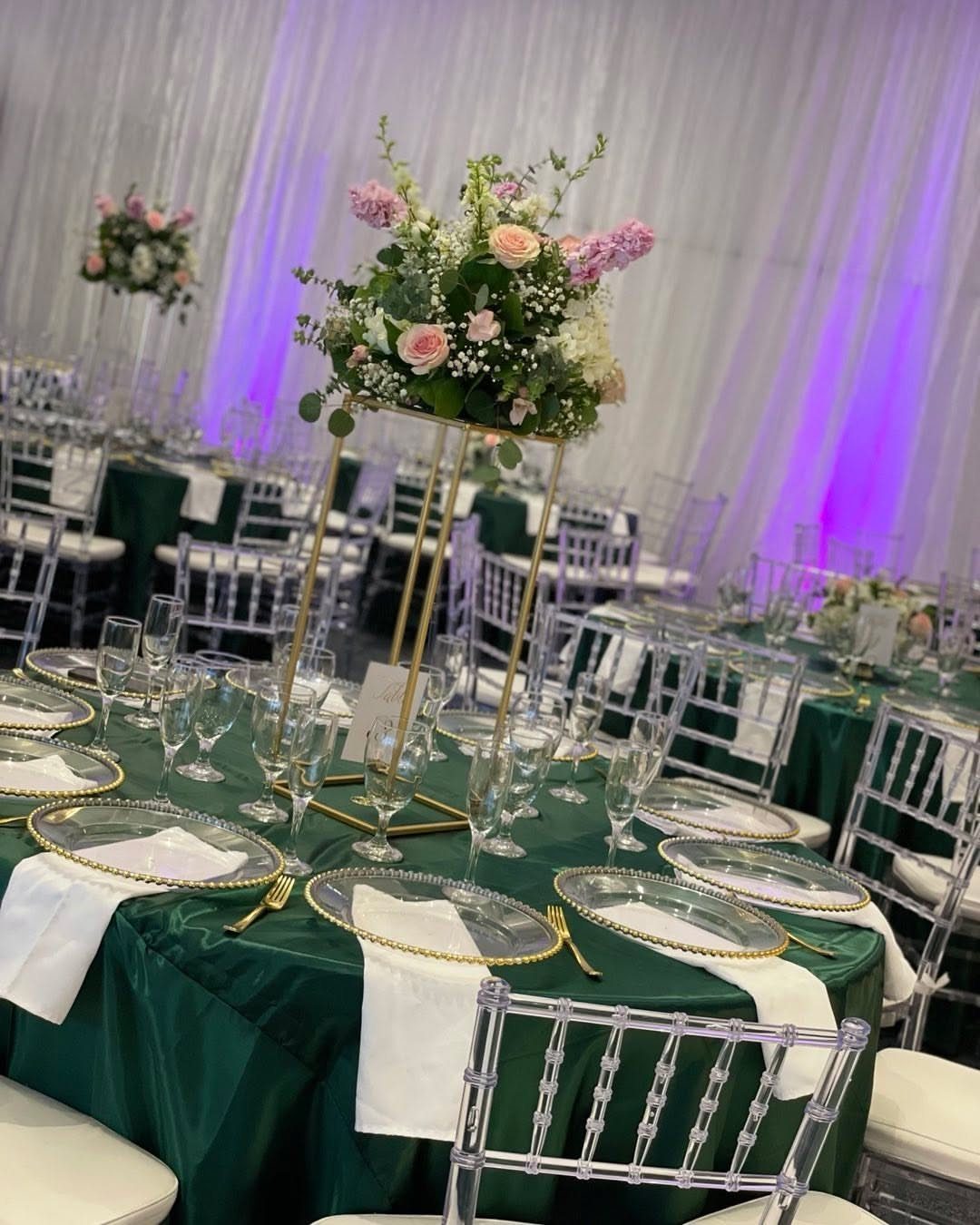Blush pink and white floral arrangement on a gold stand over emerald green linens