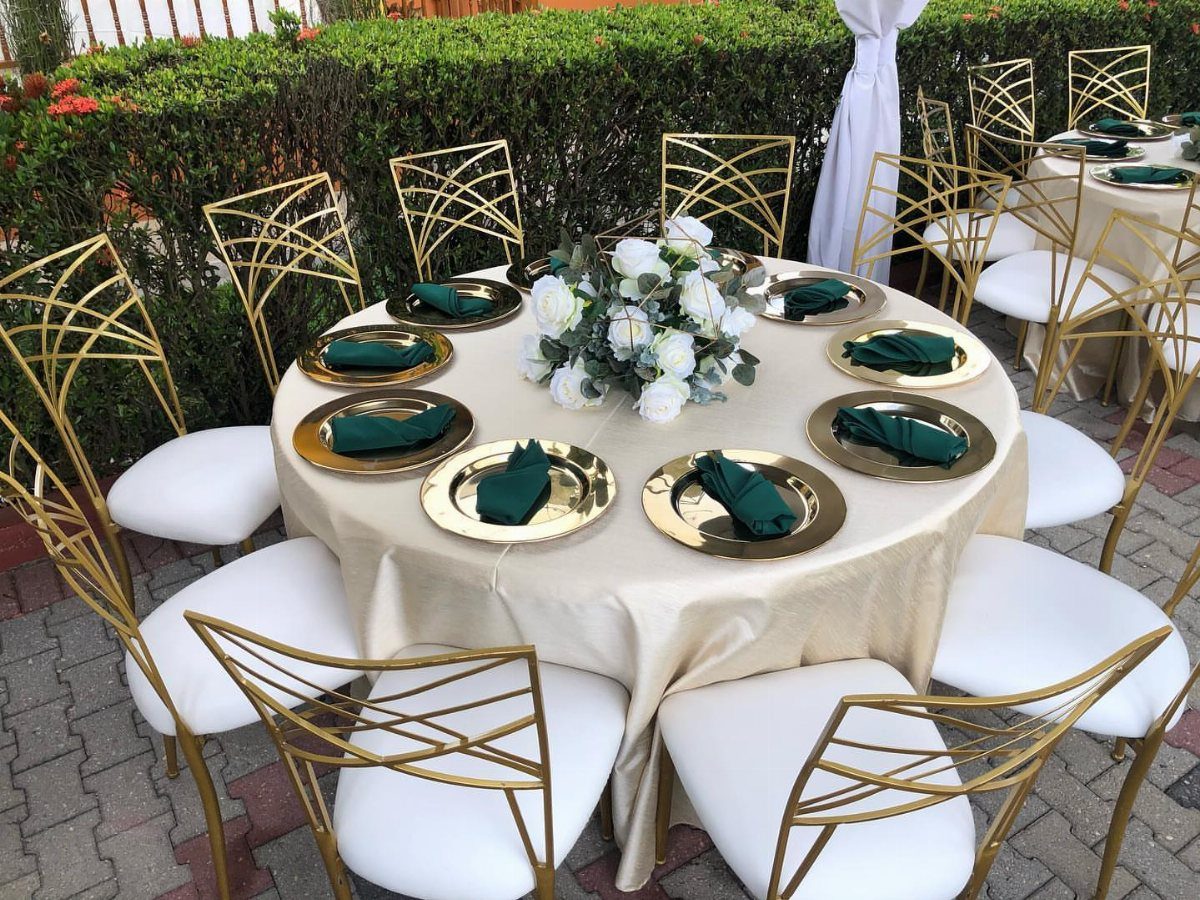 Champagne tablecloth with gold charger plates, emerald green napkins, and white floral centerpiece.