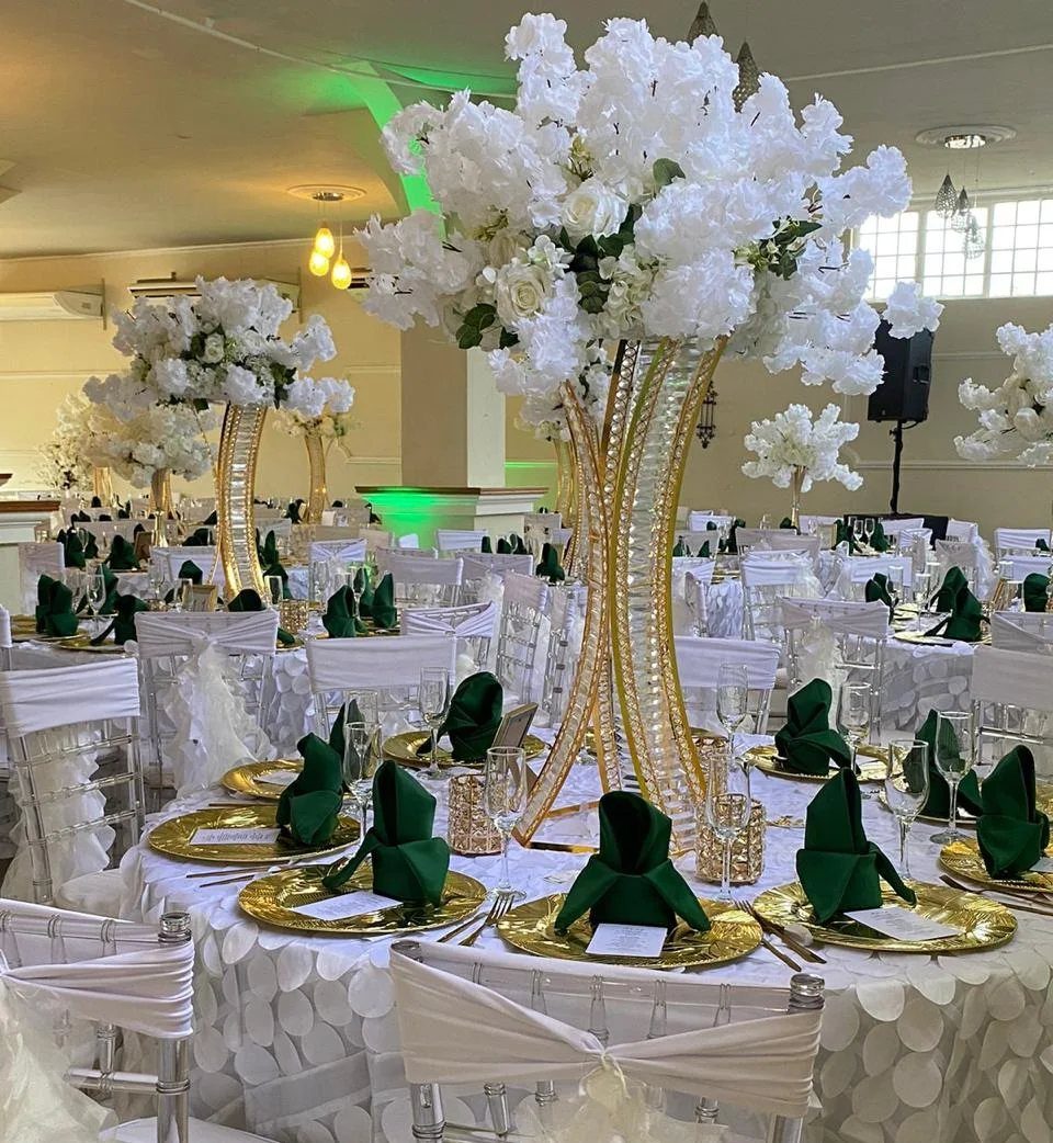 Wedding table with white textured linens, gold plates, and emerald green napkins.