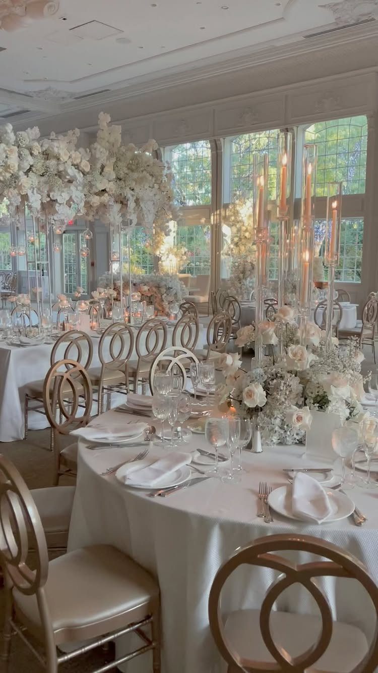 White floral centerpieces with tall gold candelabras on white wedding reception tables.