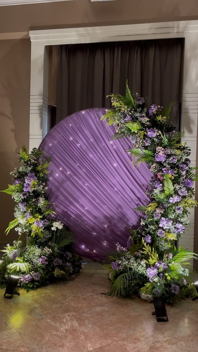 Circular purple draped backdrop with twinkling lights and floral arrangements for wedding photos.