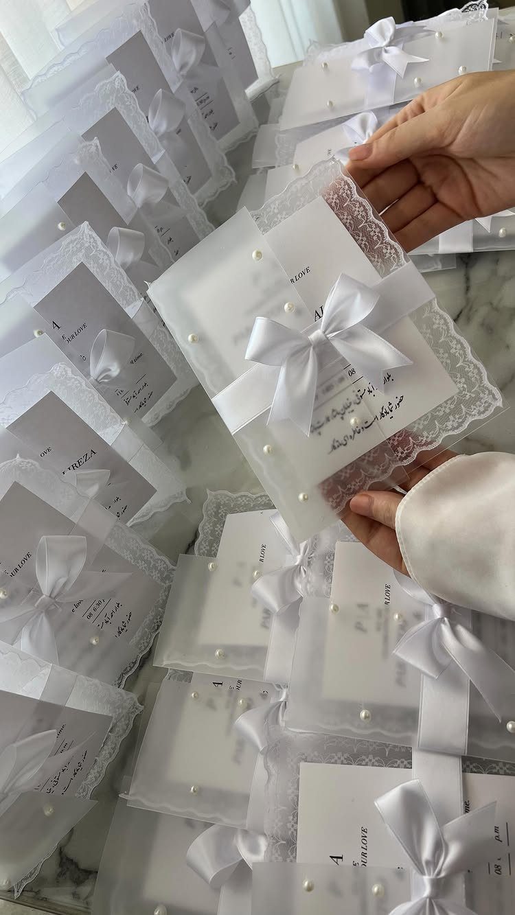 White wedding invitations with satin bows, lace trim, and pearl accents.