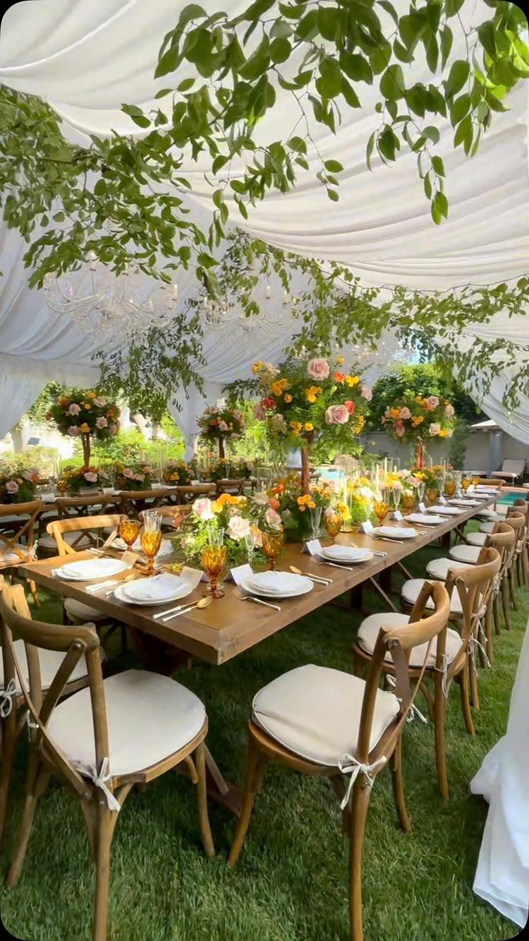 Outdoor wedding table under a white canopy with hanging greenery and floral centerpieces.