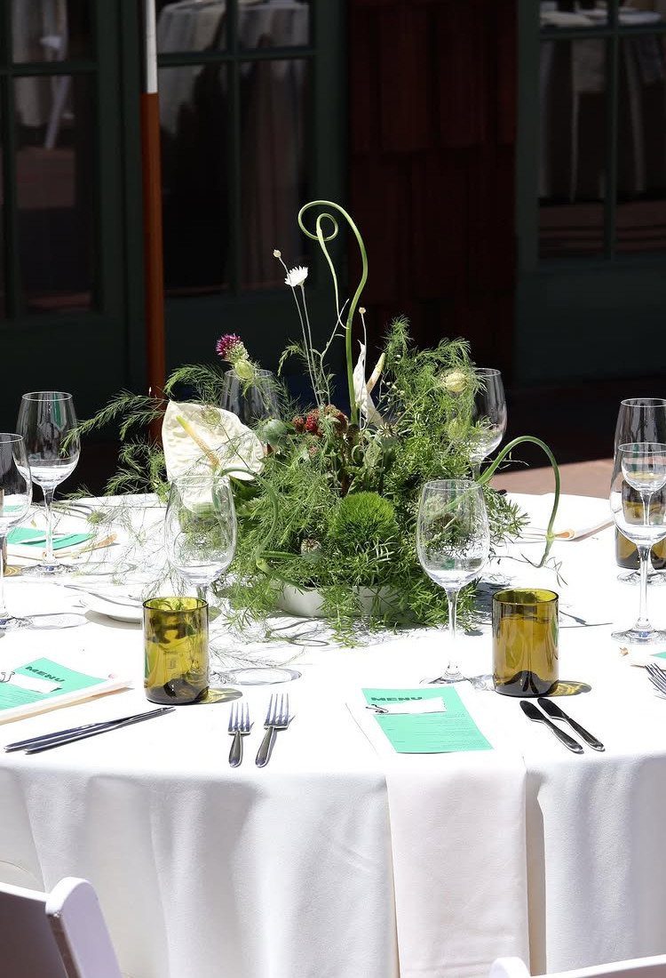 Green floral centerpiece with curly vines on a white wedding table setting