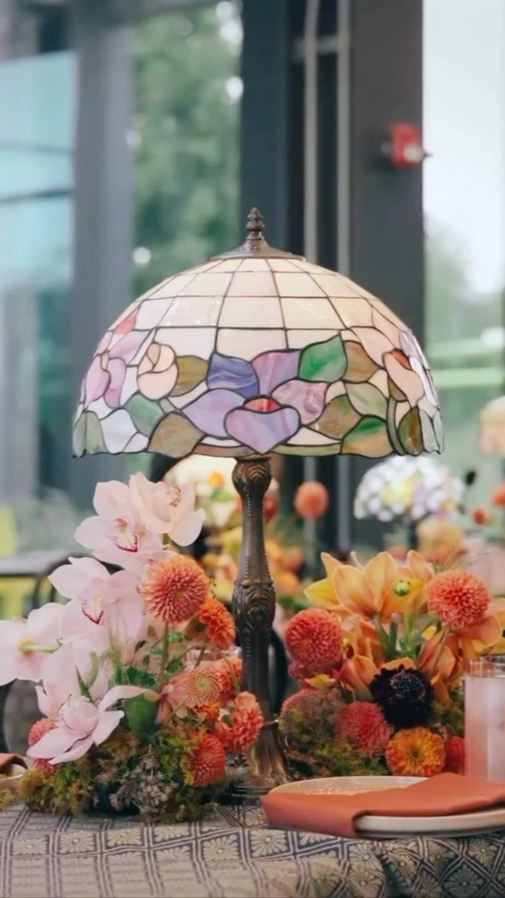 Stained glass lamp surrounded by orange and pink autumn flowers as a centerpiece.