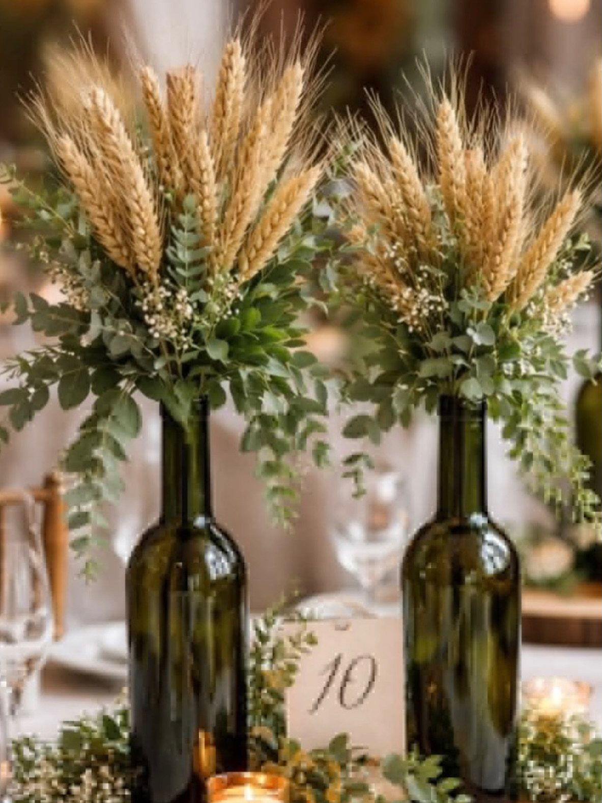 Wheat stalks and eucalyptus leaves in dark green glass bottles on a wedding table