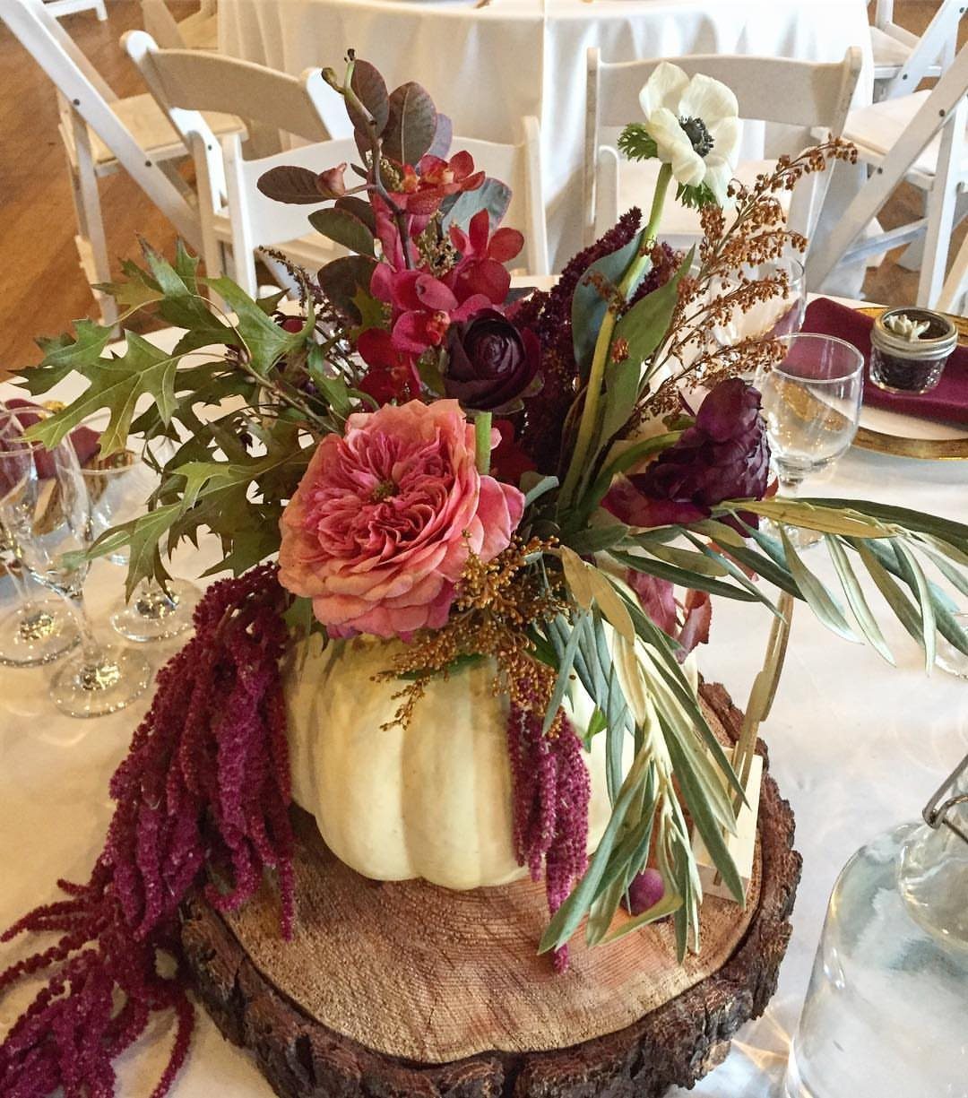 White pumpkin vase with pink and burgundy flowers on a rustic wood slice.