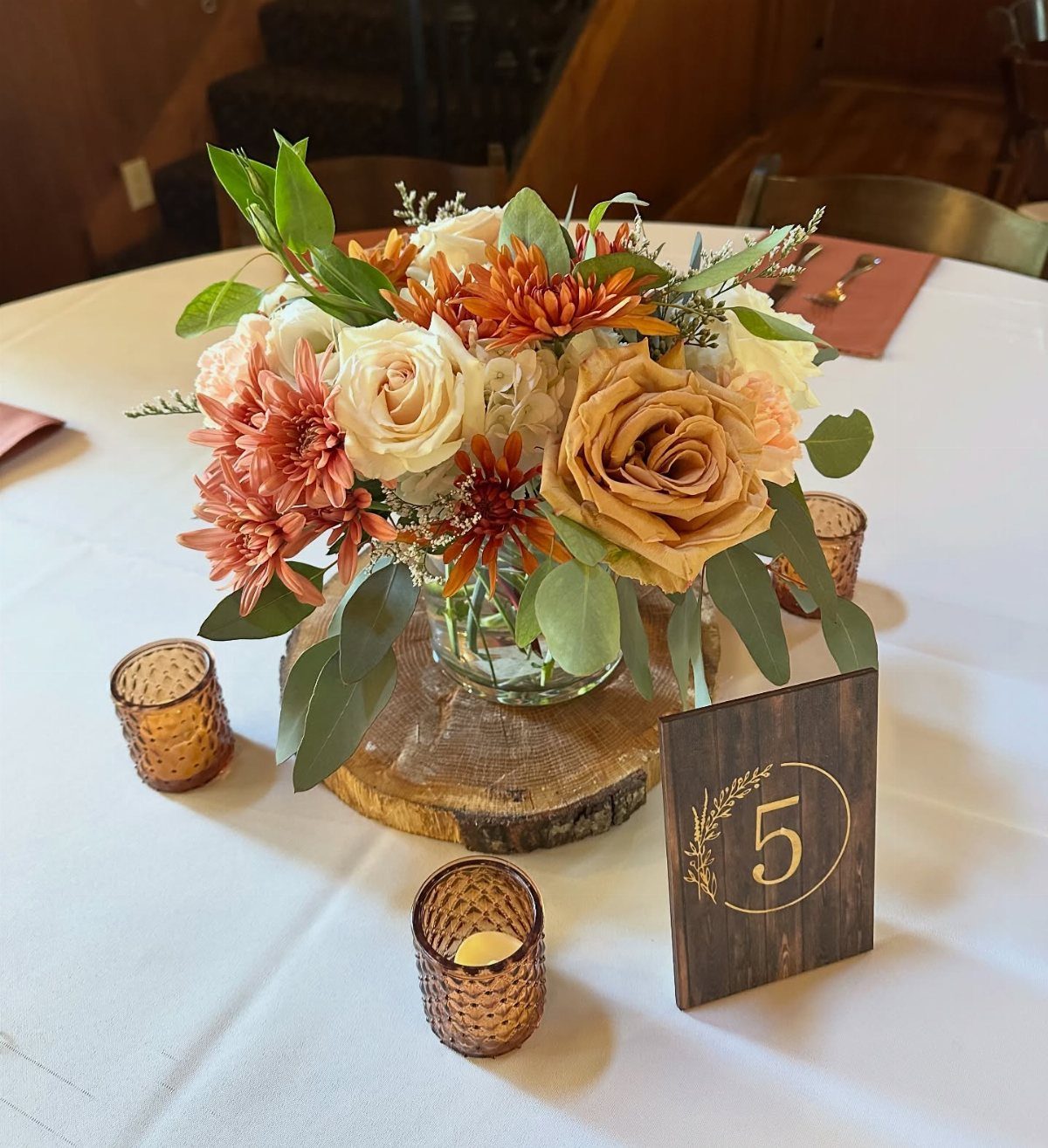 Autumn floral centerpiece with orange roses on a wooden slice with amber votives