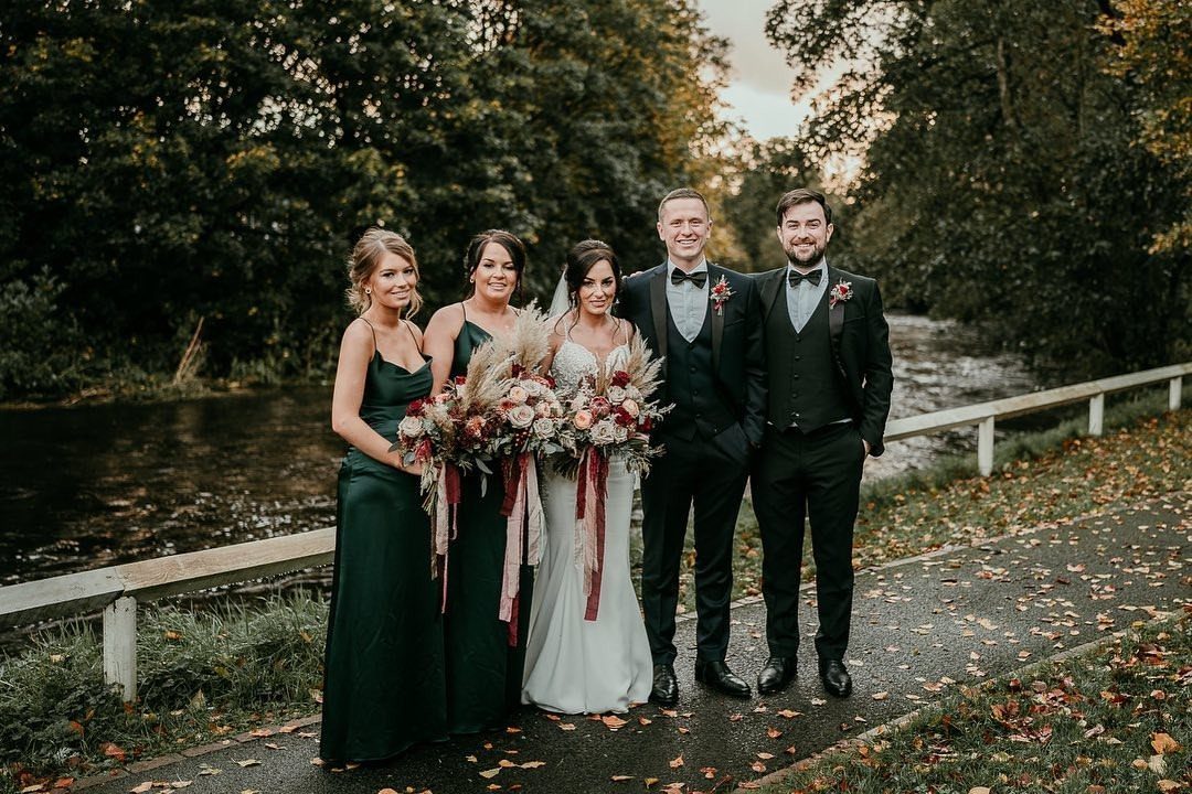Wedding party posing outdoors with emerald green bridesmaid dresses and dark suits.
