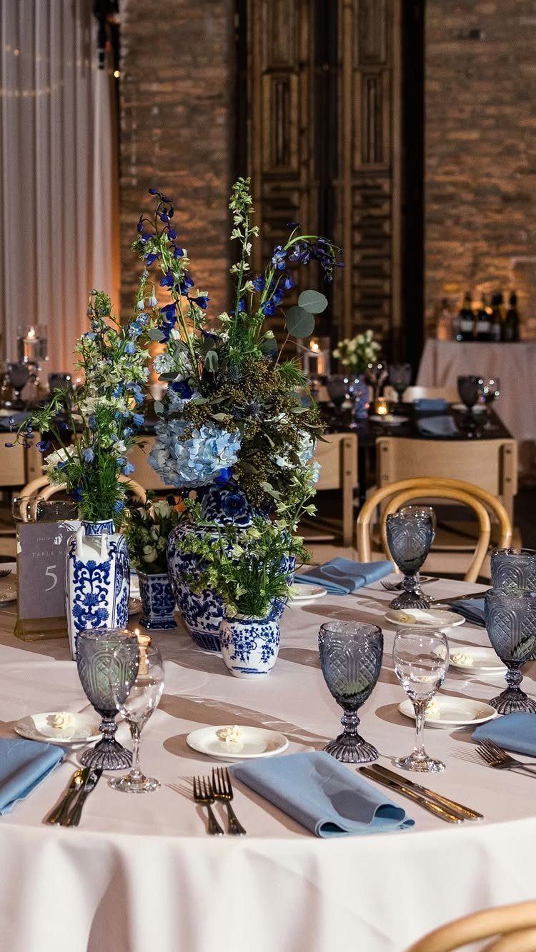 Blue and white floral arrangements in patterned vases on a wedding table.