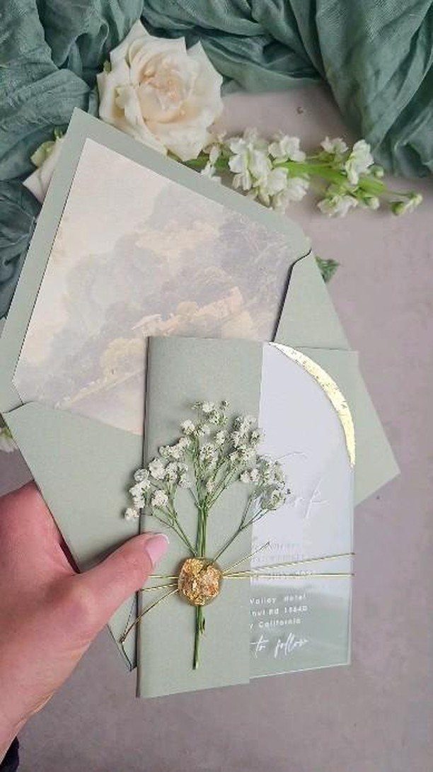 Sage green wedding invitation with a gold wax seal and white baby's breath.
