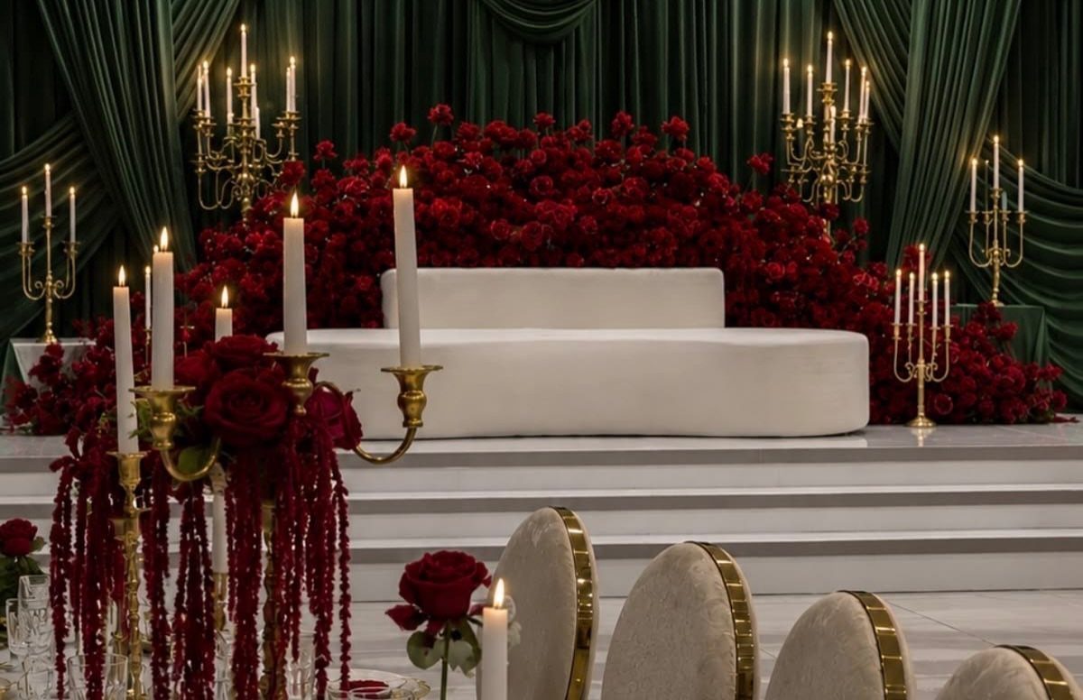 White sofa surrounded by red roses and dark green velvet curtains with gold candelabras.