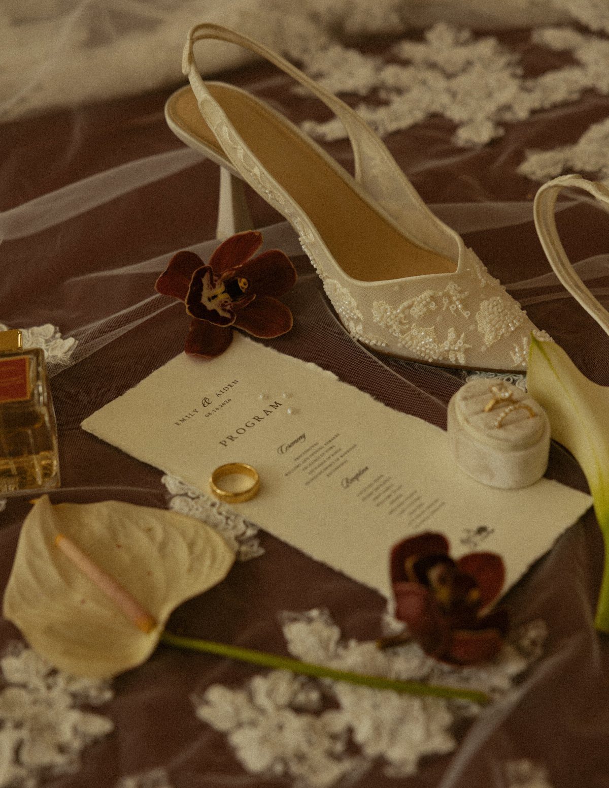 Bridal shoe and wedding program with dark red orchids on brown fabric.