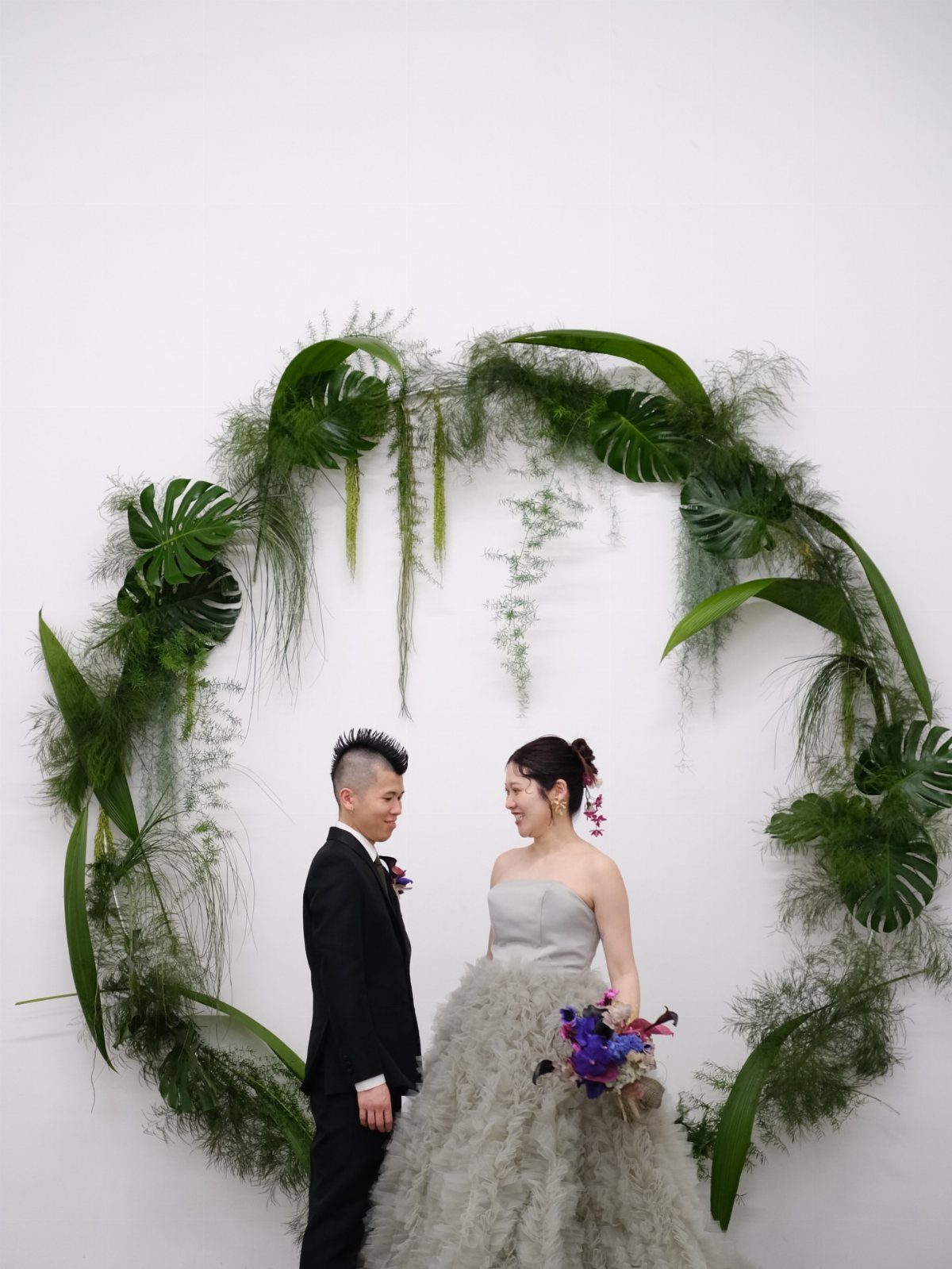 Couple posing before a circular greenery arch with a grey wedding dress