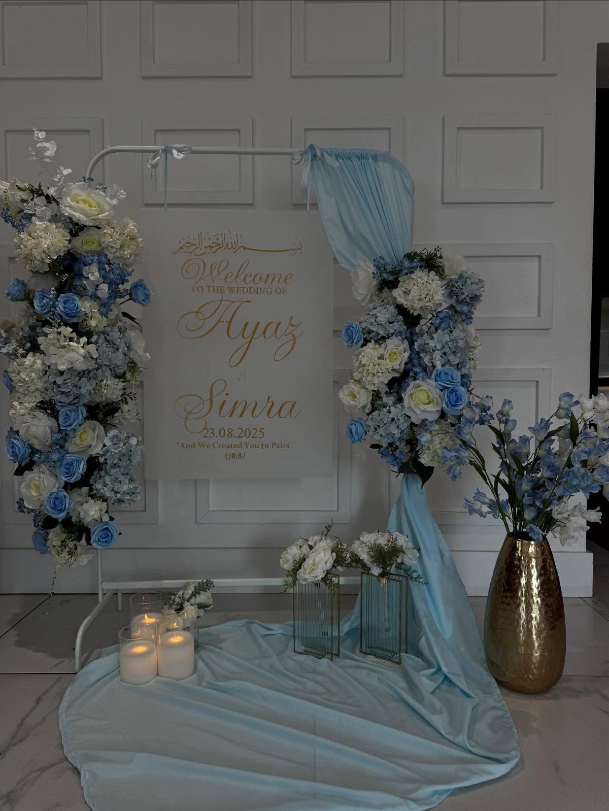 Wedding welcome sign decorated with light blue and white flowers and flowing blue fabric.