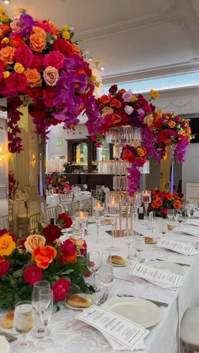 Vibrant pink, red, and orange floral centerpieces on a white wedding banquet table.