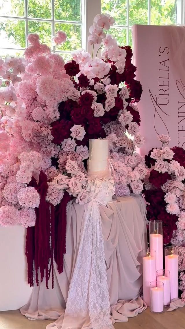 Pink and burgundy floral arrangements with a white cake and pink pillar candles.