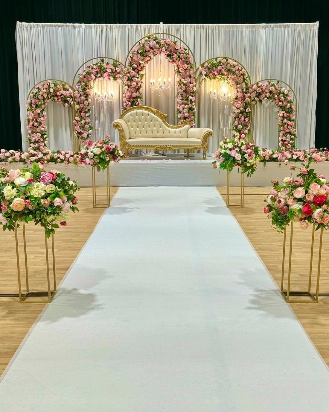 Five curved floral arches with pink roses and a gold chaise lounge.