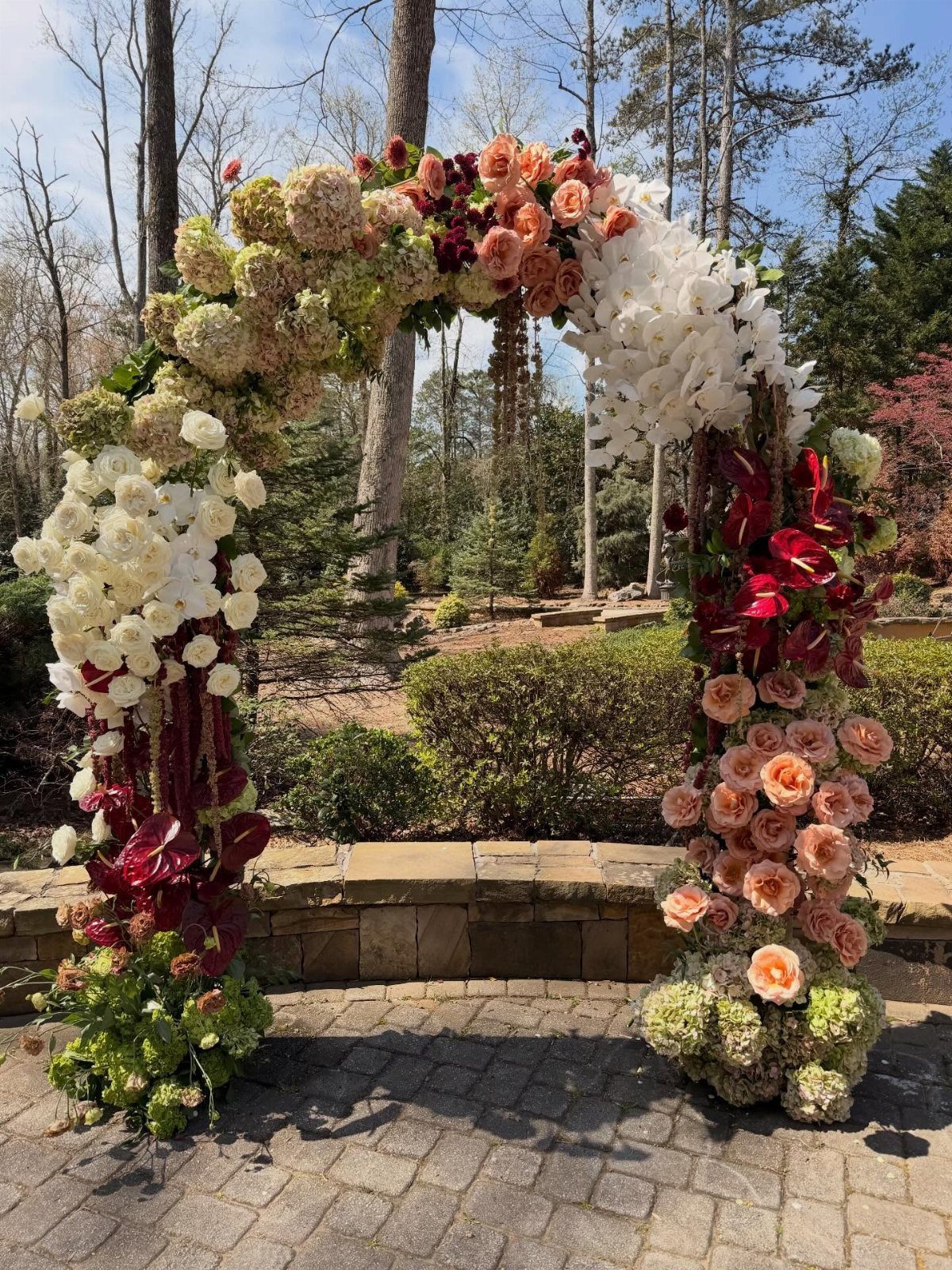 Floral wedding arch with white, peach, and red roses on a stone patio.