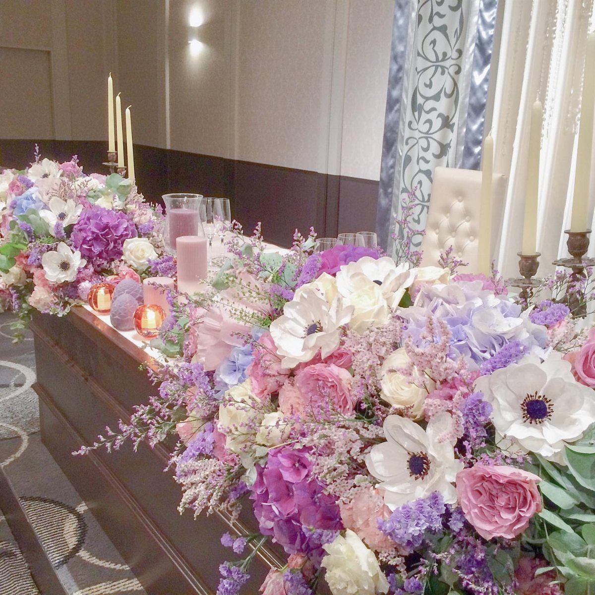 Floral table runner with purple and pink flowers and white candles at wedding