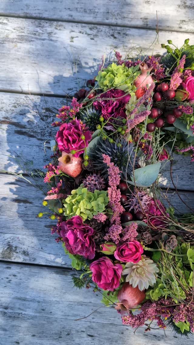 Floral wreath with magenta roses and green hydrangeas on grey wooden planks
