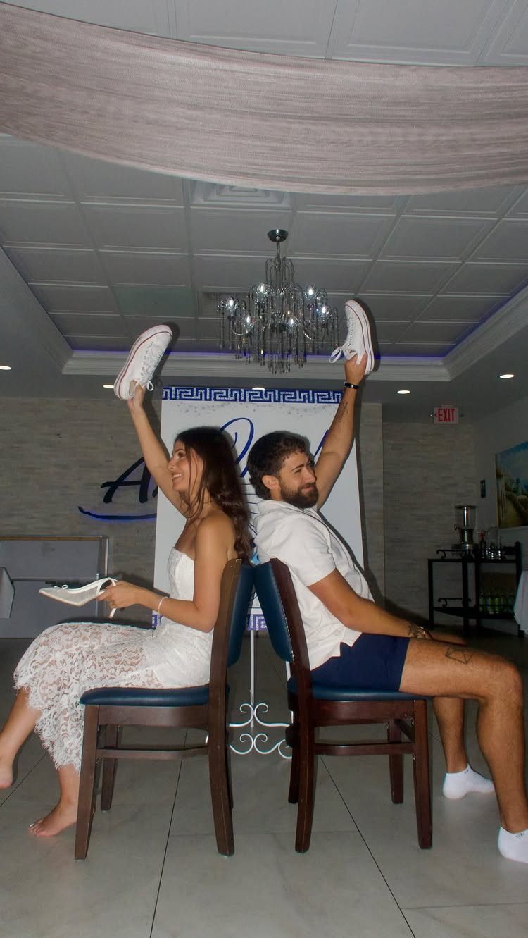 Couple sitting back-to-back holding up white shoes during a wedding shoe game activity.