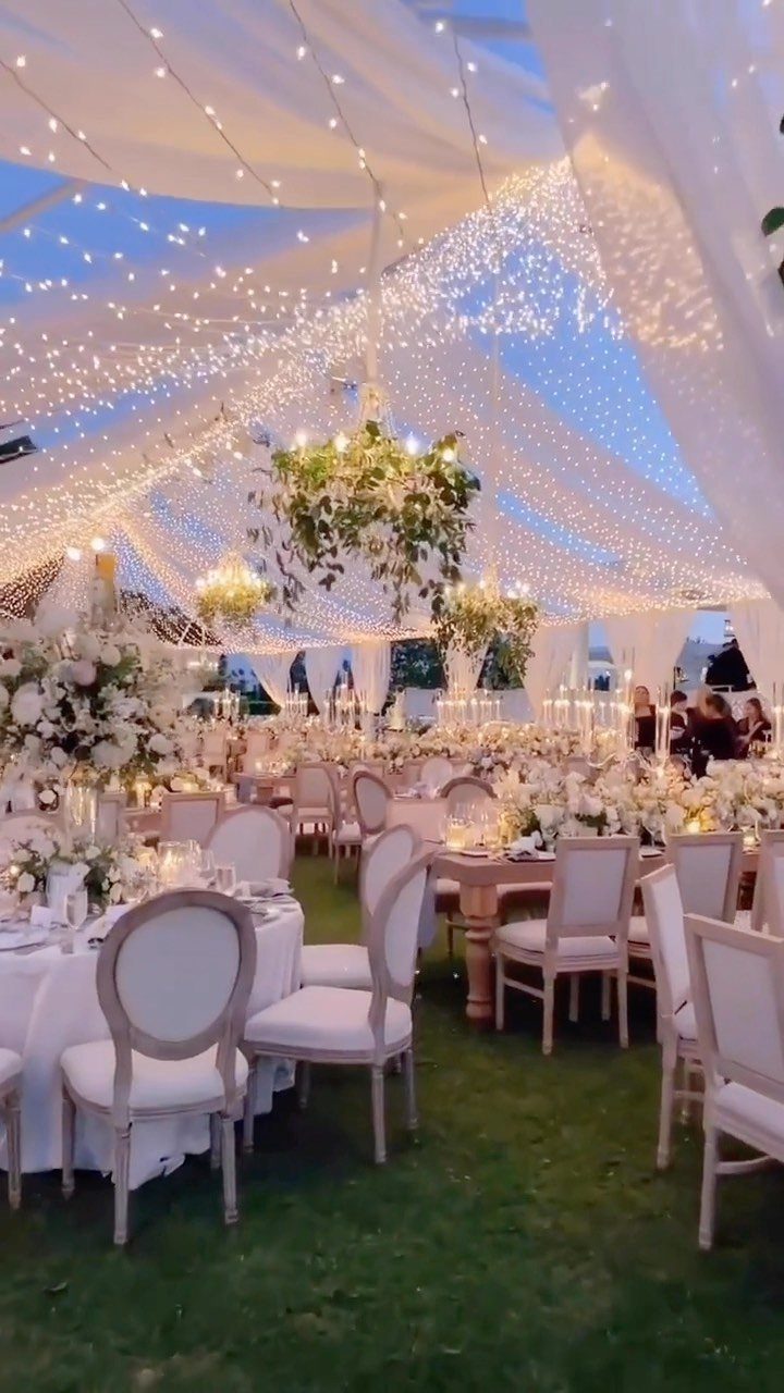 Wedding reception under a white canopy with glowing fairy lights and floral centerpieces.