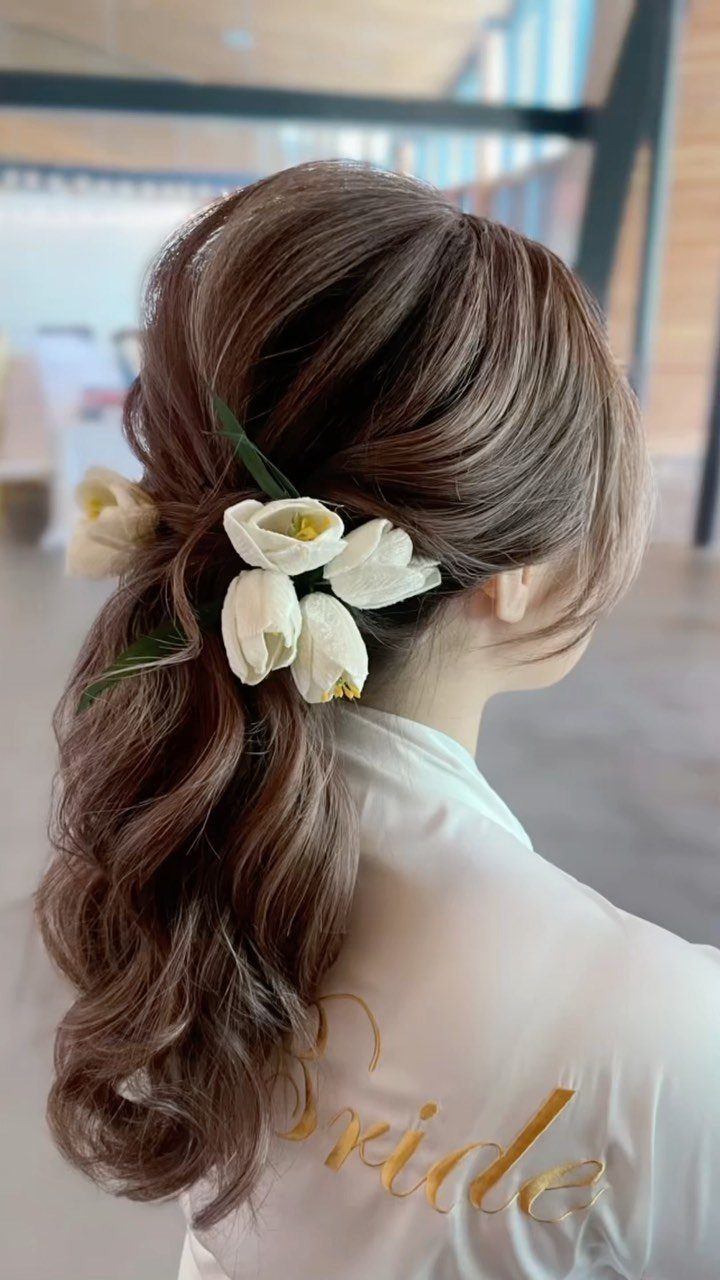 Woman's brown wavy hair styled with white tulip floral hair accessories and bridal robe.