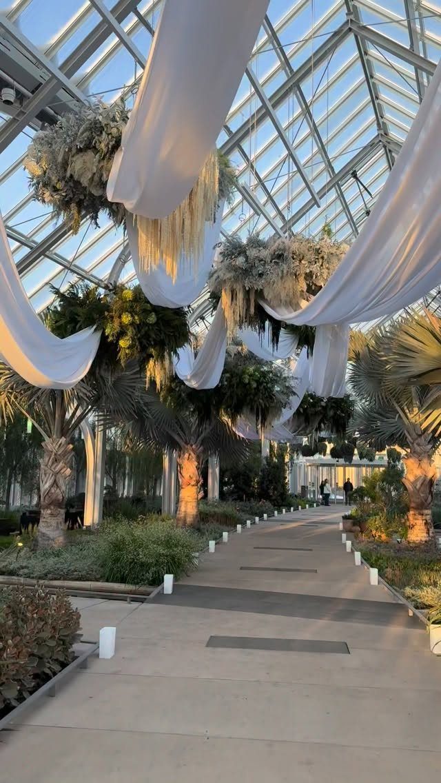 Glass greenhouse walkway with white fabric draping and hanging floral arrangements