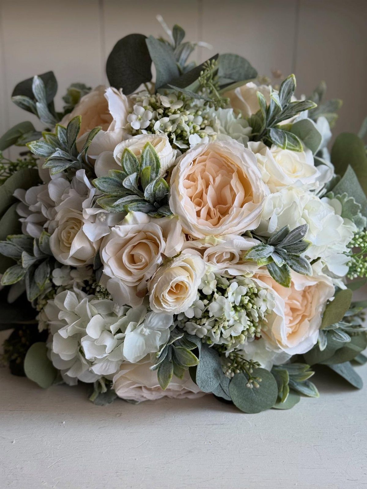 Bridal bouquet with peach roses, white hydrangeas, and silvery dusty miller foliage.