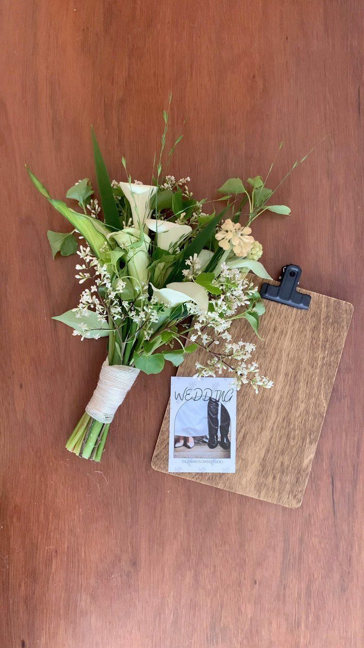 Wedding bouquet with white lilies and greenery on a wooden table with photo