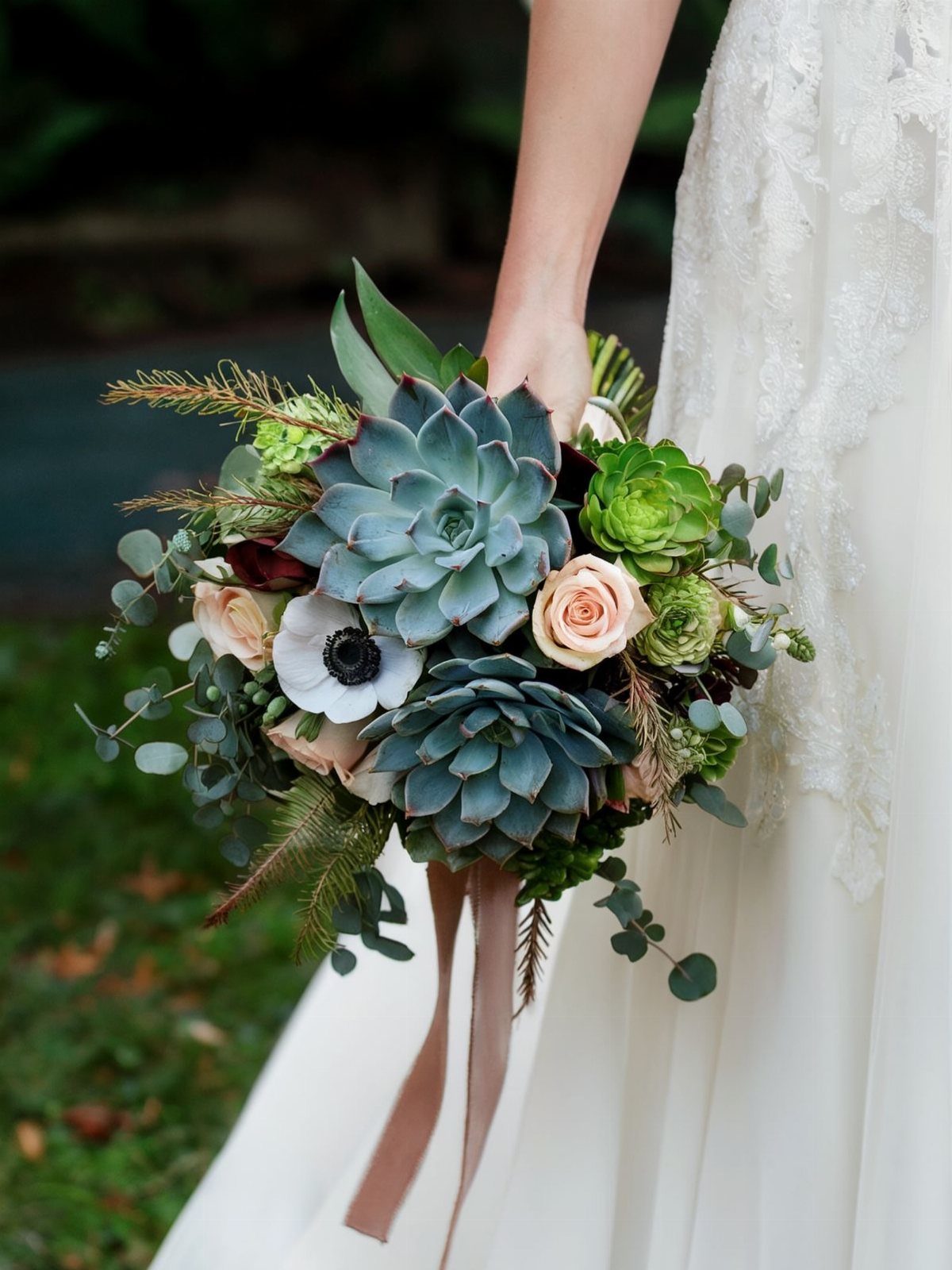 Wedding bouquet with large blue-green succulents, white anemones, and peach roses.
