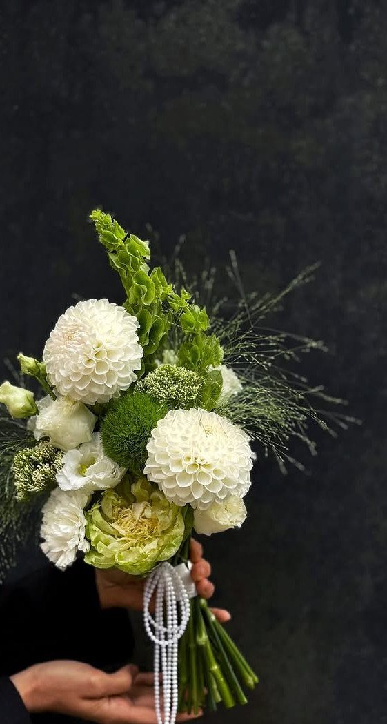 Wedding bouquet with white dahlias and green foliage tied with pearl beads.