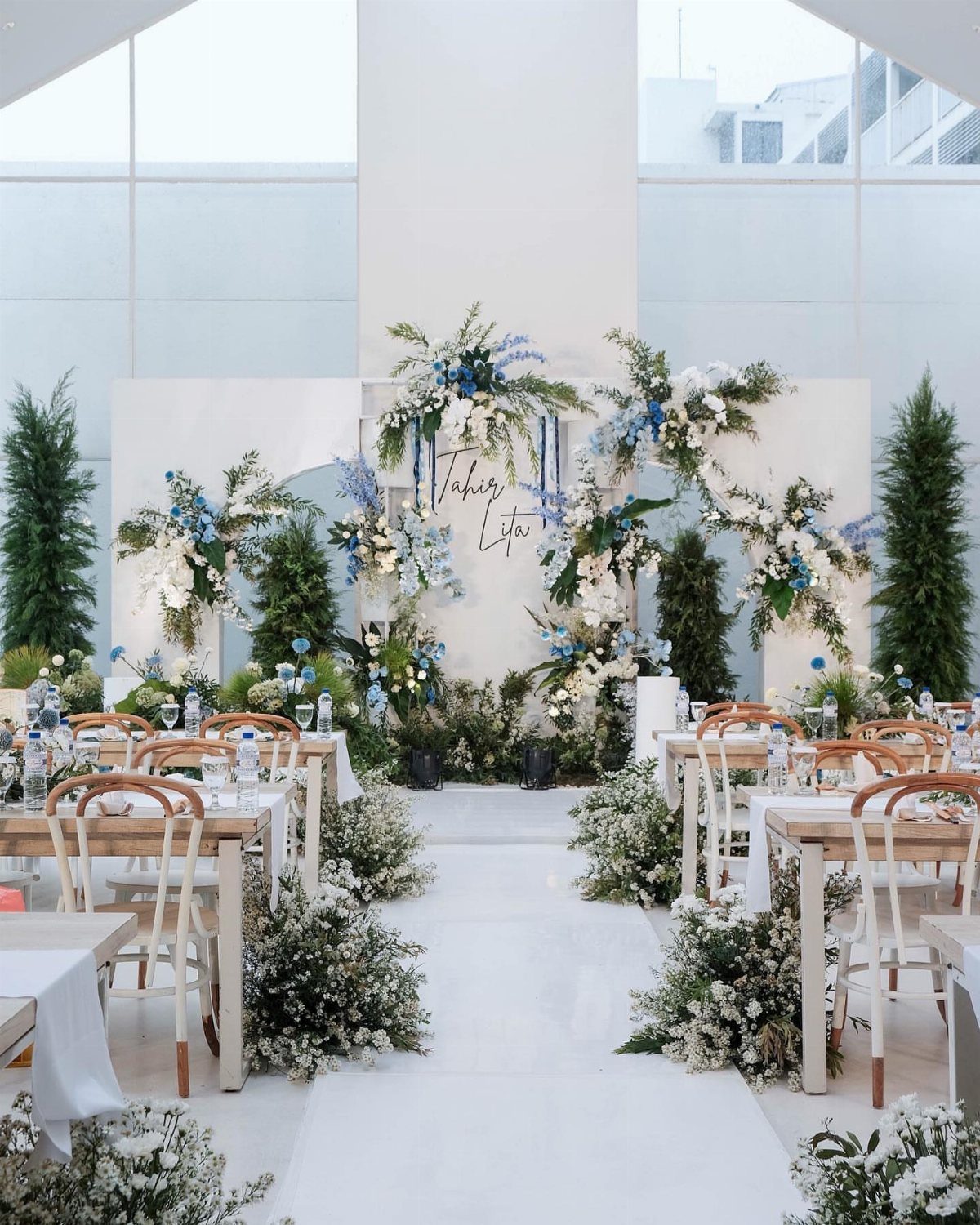 Wedding reception with white tables, blue and white flowers, and sage green foliage.