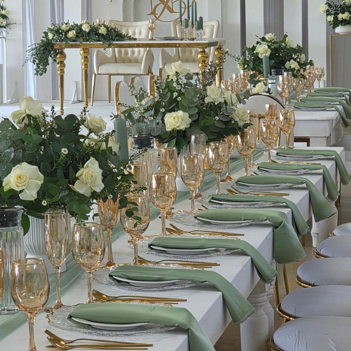 Wedding table setting with white linens, sage green napkins, and white rose centerpieces.