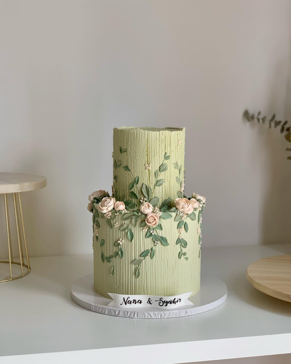 Two-tier sage green ribbed cake decorated with pale pink roses and green vines.