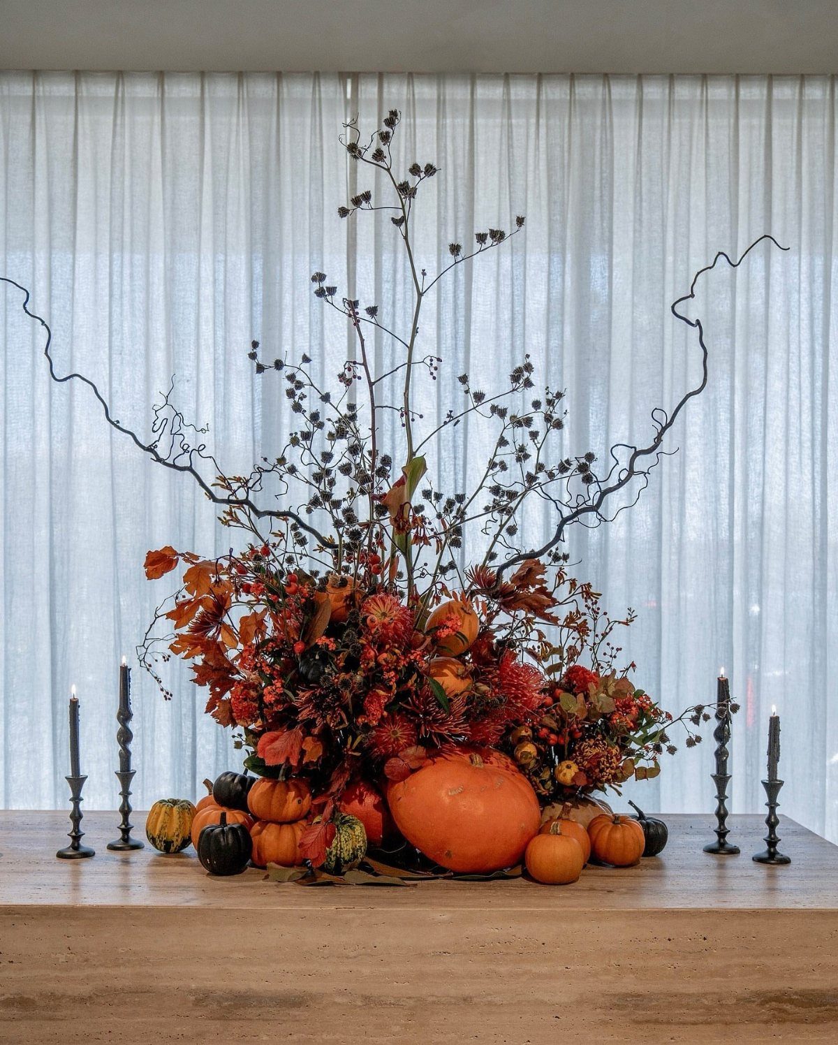 Autumnal centerpiece with pumpkins, fall foliage, and dark branches flanked by black candles.