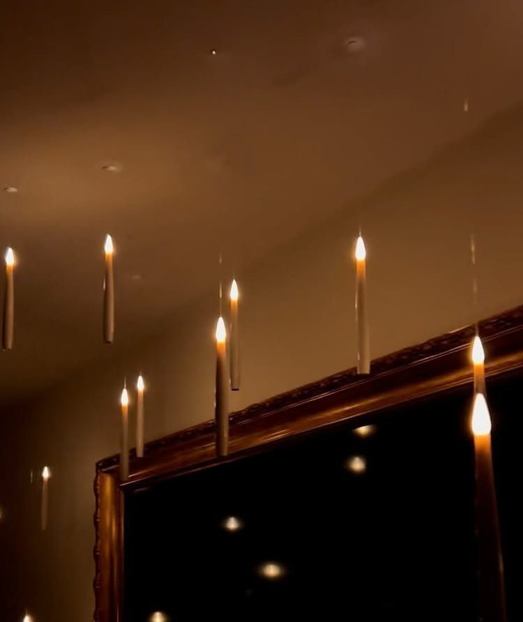 Lit white taper candles hanging from a ceiling above an ornate gold mirror.