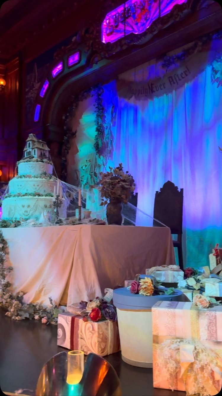 Wedding reception table with a tiered cake and blue purple atmospheric lighting.