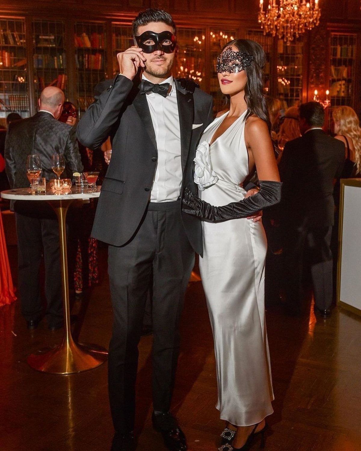 Couple in formal attire wearing black masquerade masks at an elegant evening event.